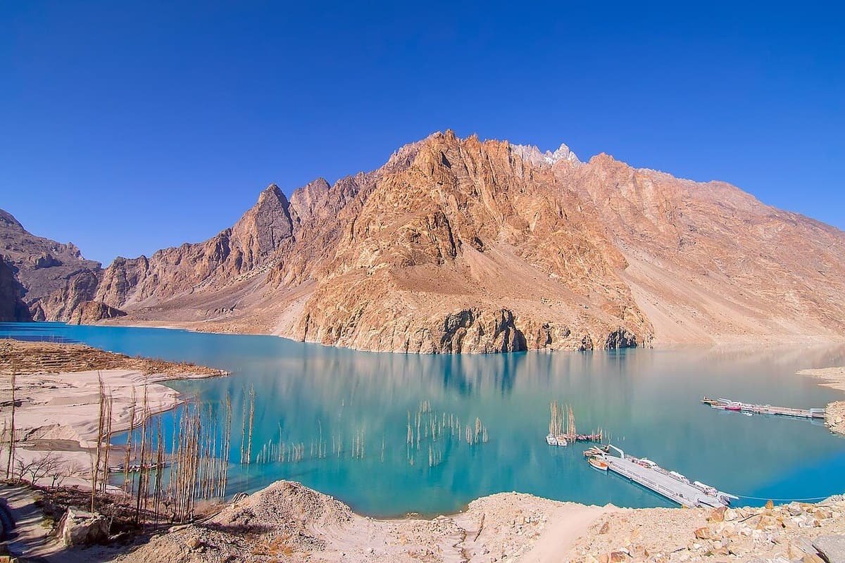 Turquoise Attabad Lake below a sunlit mountain, with boats and ferry pontoons at the jetty