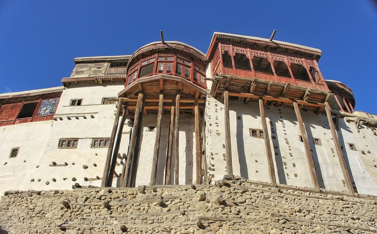 Whitewashed walls and carved red wooden balconies of Baltit Fort rise above a stone terrace under a deep blue sky.