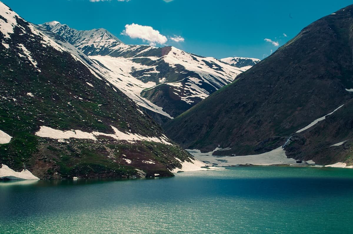 Green Lulusar Lake between steep slopes with snow patches, under a blue sky
