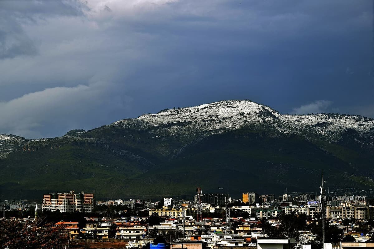 Snow-dusted Margalla Hills rise under dark storm clouds above the rooftops and buildings of Islamabad.
